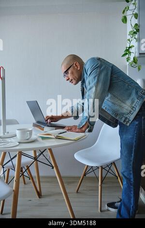 Man using laptop and notebook while leaning during remote work Stock Photo