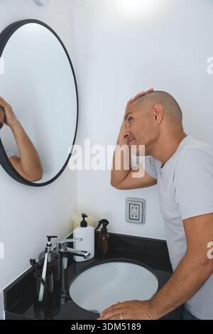 Man checking his scalp in the bathroom mirror, concerned about hair loss Stock Photo