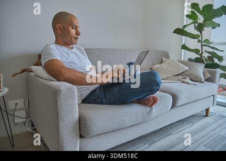 Man sitting on couch using laptop, embracing remote work and comfortable lifestyle Stock Photo