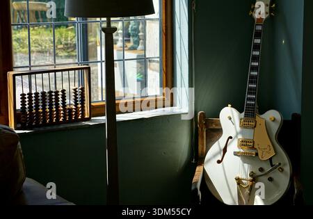 Semi hollow white guitar on a chair in corner of a rustic modern room with abacus and lamp. Window lets in natural light Stock Photo