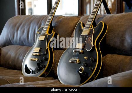 Two black guitars with yellow binding on a leather sofa with a large mirror in the background Stock Photo