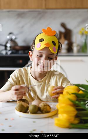 Smiling child wearing bunny ears with natural Easter eggs at home kitchen Stock Photo