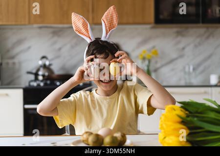 Smiling child wearing bunny ears with natural Easter eggs at home kitchen Stock Photo