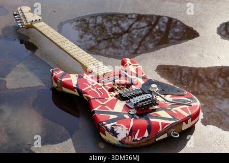 Iconic striped guitar on a skate ramp with worn surface complementing the look and vibe of the guitar. Puddles and reflection in background Stock Photo