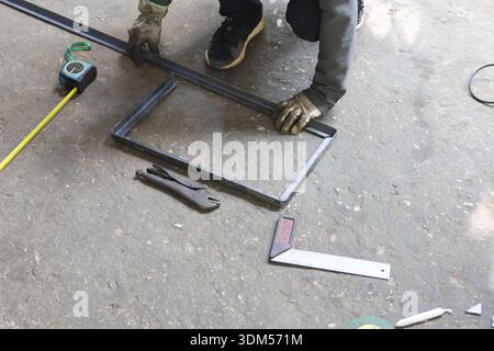 Skilled worker showing intense concentration while making metal frame. industrial workshop setting highlights manual labor, craft, skill, and tools in Stock Photo