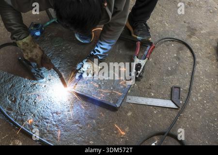 Focused welder at work using equipment for metal fabrication in an industrial factory. intense welding process creates bright sparks, highlighting man Stock Photo
