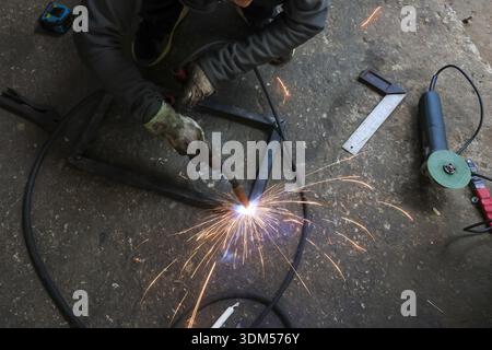 Focused welder working with welding tool, joining metal in workshop. Sparks fly from bright arc, showing craftsmanship and manual labor in fabrication Stock Photo