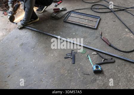 Worker in workshop measuring long steel bar. man with caliper and tape showing precision metalwork with focus and concentration on industrial floor Stock Photo
