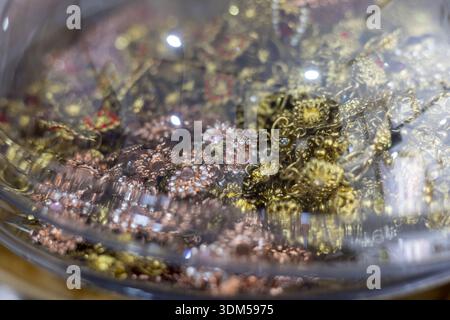 Close up view of precious gold and copper metal powder or flakes inside clear glass container. This valuable raw material looks shiny and intricate, r Stock Photo