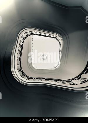 Abstract black and white view looking up through a curved stairwell with ornate railings and strong architectural symmetry Stock Photo