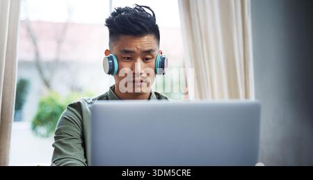 Headphones, programming or asian man with laptop for remote work, system maintenance or development. Tech, freelancer or developer in home for Stock Photo