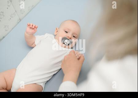 Baby falls asleep lying in crib, surrounded by mother's gentle touch. Infant is surrounded by affection and tender care, in loving arms of its parents. Baby care, guardianship Stock Photo