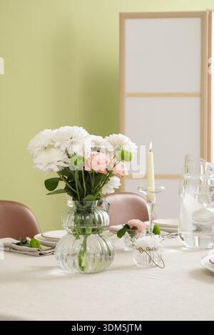 Stylish table setting with wedding decorations near green wall in dining room Stock Photo