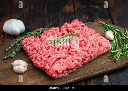 Fresh raw groundmeat with rosemary and thyme on dark wooden board over rustic table ideal for cooking, butcher and protein ingredient themes Stock Photo