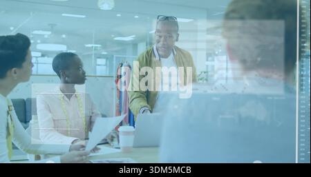 Pointing mature man leaning and directing toward laptop at design studio table, with measuring tape Stock Photo