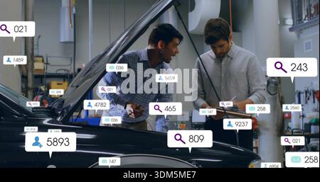 Inspecting black car in garage, two techs leaning into hood, noting on clipboard with overlay icons Stock Photo