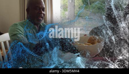 Smiling senior man in green shirt reaching for bowl of rolls at dining table, blue overlay Stock Photo