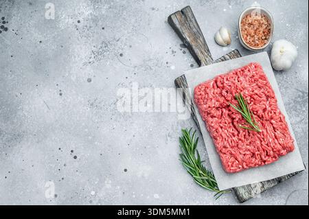 Fresh raw ground mince beef meat with rosemary on parchment over rustic wooden board and concrete background ideal for cooking and protein visuals Stock Photo