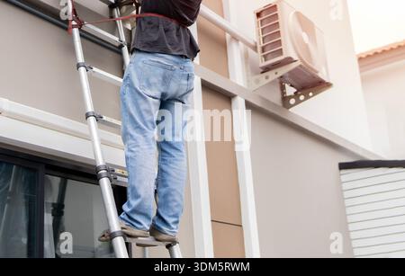 Worker climbing up metal ladder on wall at outdoor, closeup. Repairman worker standing on ladder.  Safety and maintenance concept. Stock Photo