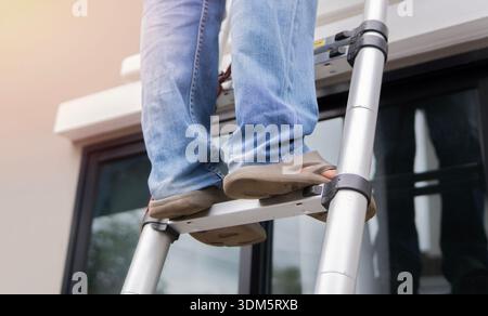 Man standing on ladder, low angle view, man climbing ladder against outdoors. Close-up. Stock Photo
