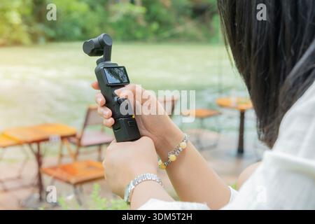 Female traveler in casual dress taking picture of beautiful stream on smart pocket camera during vacation. Tourist during holidays. Stock Photo