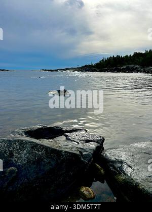 Dramatic sky over calm Baltic Sea with rocky pine-covered headland along the Swedish coastline Stock Photo