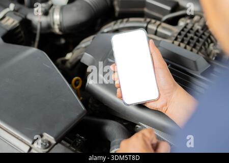 Close up hand using mobile phone with blank screen with broken car. Phone on mechanic hand holding in car repair shop. Copy space. Stock Photo