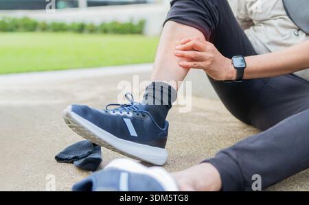 Cropped shot of elderly sportsman jogging outdoor at park, sitting on the ground and touching his leg, retired athletic man suffer from shin splint, c Stock Photo