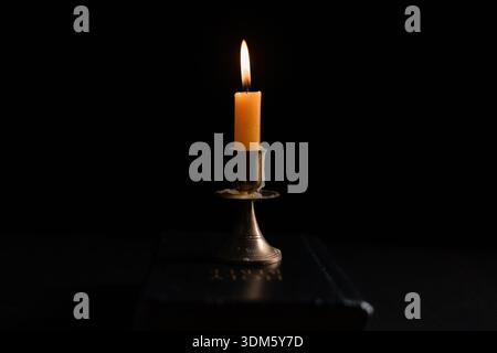 Dark, an antique candle cast its light on the old Bible, its flames flickering gently over the book on the table, symbolizing the enduring essence of Stock Photo