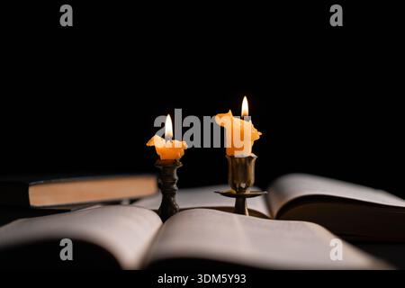 Dark, an antique candle cast its light on the old Bible, its flames flickering gently over the book on the table, symbolizing the enduring essence of Stock Photo