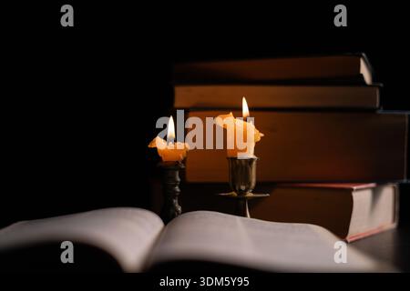 Dark, an antique candle cast its light on the old Bible, its flames flickering gently over the book on the table, symbolizing the enduring essence of Stock Photo
