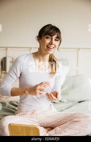 Woman applying lotion on her hand, smiling and doing a beauty self care routine at home Stock Photo