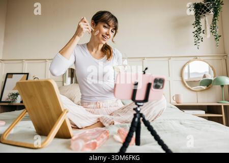 Woman recording a skin care tutorial with a facial roller and enjoying self-care Stock Photo