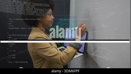 Writing woman in tan blazer drawing code on whiteboard in office, holding laptop, marker, HUD Stock Photo