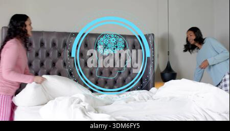 Holding pillow, two women in pajamas adjusting king-size bed in bedroom, with holographic blue head Stock Photo