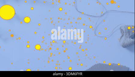 Scattering bright yellow dots covering pale blue tabletop, with ball of twine and stacked paper Stock Photo