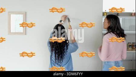 Hanging women mounting art on wall, holding hammer, in blue, pink tops, showing orange dollar signs Stock Photo