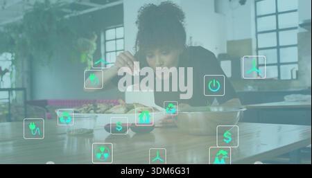 Plating chef in jacket leaning over wood table, kitchen, garnishing plated dish showing eco icons Stock Photo