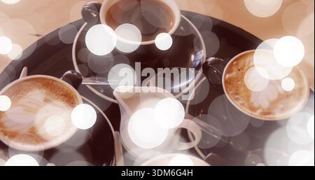 Displaying dark tray holding four coffee cups with latte art, milk jug, teaspoons on cafe table Stock Photo