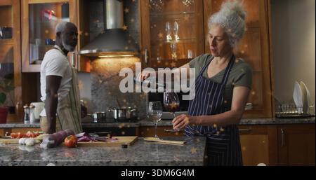 Pouring woman in striped apron filling wine glass at home kitchen island, with cutting board Stock Photo