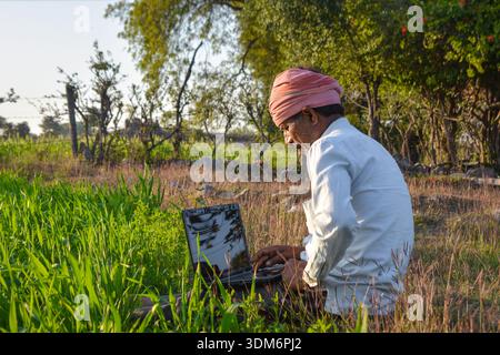 Indian rural man using laptop at agriculture field. Modern technology in agriculture Stock Photo