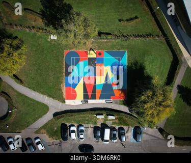 Ferney-Voltaire, France - 21 September 2024: Aerial view of a vibrant basketball court, a mosaic of geometric shapes in bold colors, nestled in a gree Stock Photo