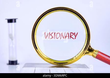 A golden magnifying glass centers on the red word visionary, placed on a white background. An hourglass and calculator indicate time and strategic tho Stock Photo