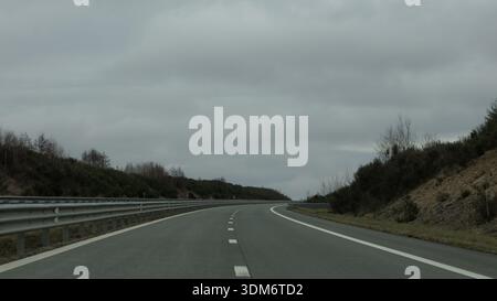 Curving empty highway through rural landscape under cloudy sky Stock Photo