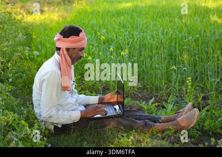 Indian rural man using laptop at agriculture field. Modern technology in agriculture Stock Photo