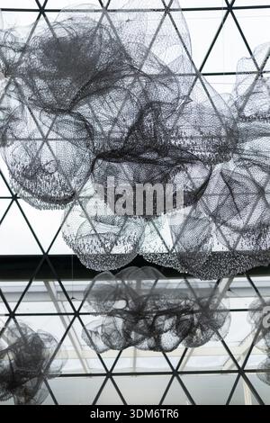 Large black mesh structures float under a geometric ceiling in an airy space. Light filters in, creating an engaging and visually interesting atmosphe Stock Photo