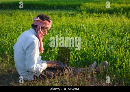 Indian rural man using laptop at agriculture field. Modern technology in agriculture Stock Photo