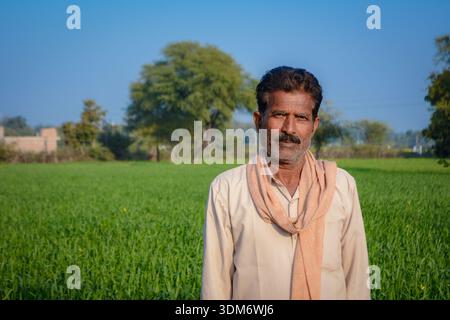 Indian farmer standing in green crop field looking at camera Stock Photo
