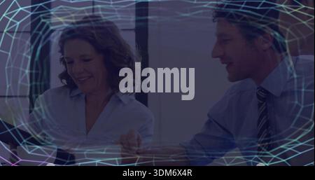 Reviewing three colleagues business-clad leaning over tablet in meeting room, with mesh overlay Stock Photo