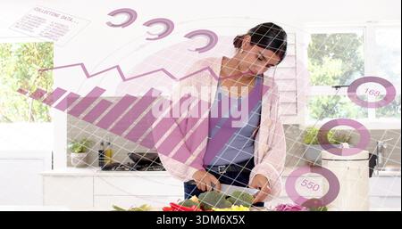 Chopping Indian woman preparing vegetables at home counter in pink cardigan with knife data overlay Stock Photo
